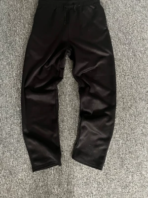 Svarta mjukisbyxor från H&M Move - Svarta mjukisbyxor från H&M Move med dragsko i midjan och elastisk resår. Byxorna har en enkel och stilren design, perfekta för chill dagar. Tillverkade i ett mjukt och stretchigt material som känns skönt mot huden.