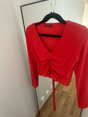 Röd croppad topp med snörning - Trendig röd croppad topp från Gina Tricot med lång ärm och v-ringning. Toppen har snygg snörning framtill som ger en rynkad effekt och kan justeras för önskad passform. Perfekt att styla med höga jeans eller kjol.