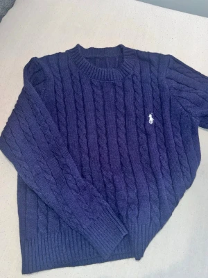 Marinblå stickad tröja Polo Ralph Lauren - Säljer en mörkblå kabelstickad tröja från Polo Ralph Lauren med klassisk vit broderad logga på bröstet.