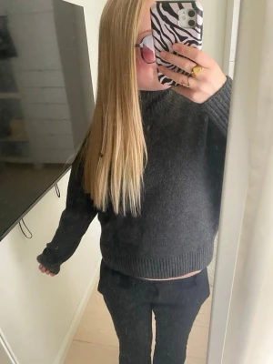 Mörkgrå stickad tröja , halv polo krage - Helt ny mysig mörkgrå stickad tröja med rund hals och ribbade muddar vid ärmslut och nederkant. Tröjan har en avslappnad passform och är perfekt för kyligare dagar. Materialet ser ut att vara mjukt och värmande, troligen ull- eller ullmix.