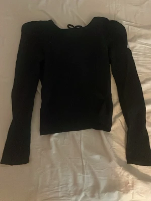 Svart långärmad topp med knyte i ryggen.  - Snygg svart långärmad topp med puffiga axlar och knyt i nacken. Ändras efter kroppsform och sitter jättefint . 