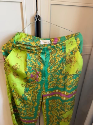Färgglada mönstrade byxor från mango - Säljer ett par leggings från Mango i starka färger med grönt och gult barockinspirerat mönster. Materialet känns glansigt och mjukt, perfekt för dig som gillar statement-plagg och vill sticka ut. Midjehög passform.