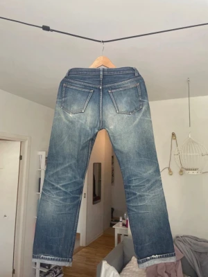 APC Selvage jeans - Säljer ett par blå jeans med raka ben och tydliga slitningar framtill. Jeansen har fem fickor, normal midja och fransade benslut för en avslappnad look. Materialet är klassisk denim i bomull. Perfekta för en casual stil.