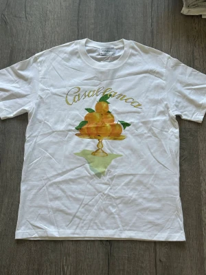 Casablanca t shirt  - Snygg vit t-shirt från Casablanca med ett färgglatt tryck av apelsiner på ett fat och loggan i gult över bröstet. Klassisk rund hals och korta ärmar. Perfekt för dig som gillar stilrena plagg med en twist.