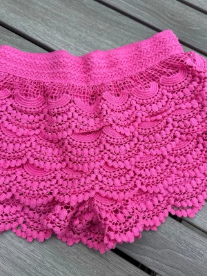 Rosa crochet shorts med volang från Gina Tricot XS 14+ teens - Säljer ett par helt nya och oanvända knallrosa/pink färgade virkade crochet shorts med volangkant och detaljerad spets från Gina Tricot. De har elastisk midja och ett unikt mönster som ger en riktigt somrig vibe. Perfekta för dig som vill sticka ut lite extra! Köpta som present till dottern men storleken passade tyvärr inte (och hon hann ta bort prislappen så gick ej att byta dem).
