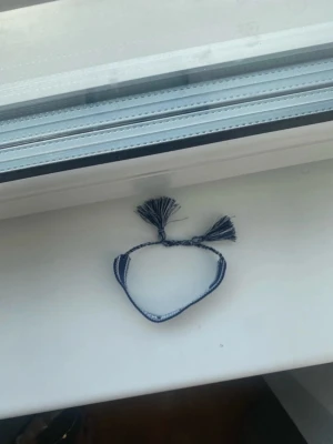 Mörkblå armband  - Snyggt blått tygarmband  med vit text och dekorativa tofsar i ändarna. Armbandet har ett vävt mönster och knyts enkelt runt handleden. Perfekt accessoar för dig som gillar exklusiva detaljer och streetstyle.