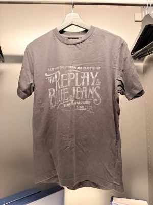  Replay  - Snygg svart t-shirt från Replay med stort vitt tryck på bröstet där det står 'Replay Blue Jeans'. Klassisk rund hals och korta ärmar. Tillverkad i mjuk bomull som känns skön mot huden. Perfekt för dig som vill ha en enkel men stilren look.