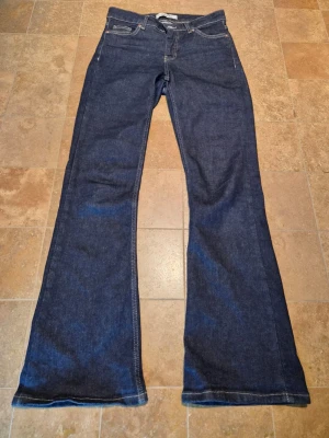 Bootcut jeans - Mörkblå bootcut jeans med bruna/beiga sömmar. Använda kanske 2-3 gånger och är i fint skick.