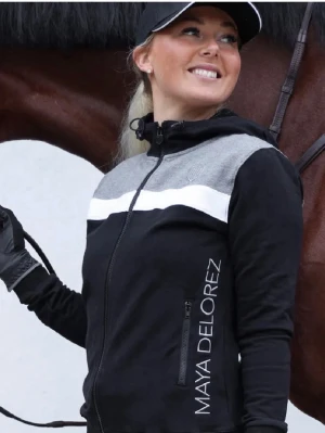 Ridtröja Maya Delorez - Snygg svart hoodie från Maya Delorez med dragkedja, grå axelparti och vit rand över bröstet. Stor logga längs sidan och huva med dragsko. Perfekt för en sportig och avslappnad stil.