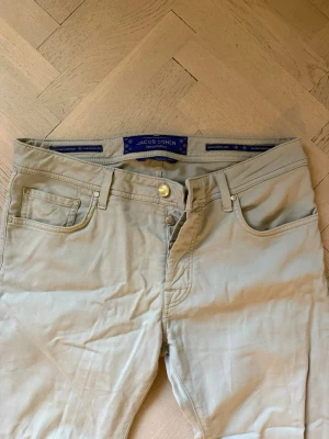 Tunna jeans från Jacob Cohen: Special edition - Snygga tunna jeans mer åt chinos hållet från Jacob Cohen med klassisk femficksdesign och raka ben. Byxorna har diskreta sömmar och silverfärgade detaljer vid fickorna. Perfekta för en stilren och avslappnad look. Materialet känns mjukt och följsamt.