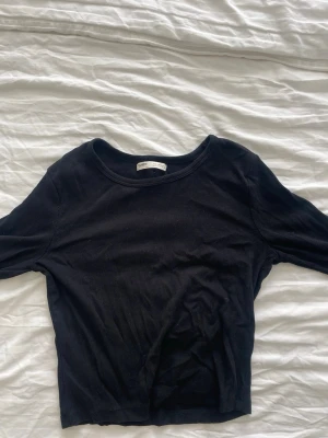 Svart ribbad topp från pull and bear - En svart ribbad topp från Pull and bear med rund halsringning och lång ärm. Modellen är croppad och har en enkel, stilren design som passar till mycket. Liten i storleken.