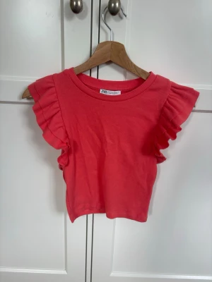 Rosa ribbad topp med volangärm Zara - Supersöt rosa topp från Zara i ribbad bomull med volangdetaljer på ärmarna. Modellen är croppad och har rund halsringning. Perfekt för dig som vill ha en färgglad och trendig topp till sommaren.