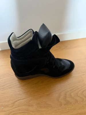 Svarta Isabel Marants - Snygga svarta höga sneakers från Isabel Marant i mocka med cool design och vadderad plös. Skorna är i storlek 39 och är bara använda 5 gånger. Säljer då dem aldrig kommer till användning