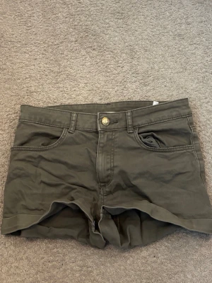 Olivgröna shorts med fickor strl 146 från H&M - Snygga olivgröna shorts med knappstängning fram. Shortsen har bälteshällor och är perfekta för varma dagar. Passformen är normal och materialet känns slitstarkt och bekvämt.