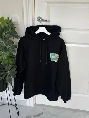 Drõle de Monsieur hoodie med spelkortstryck - Drõle de Monsieur hoodie med huva och dragsko, från Brue. På bröstet och ryggen finns tryck med spelkort i grönt, vitt och gult. Hoodien har en klassisk känguruficka framtill och är tillverkad i mjukt material, perfekt för en avslappnad streetwear-look.