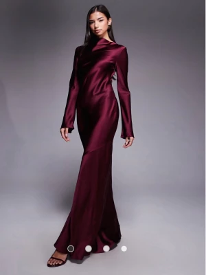 Vinröd långklänning i satin - Elegant vinröd långklänning i glansigt satinmaterial med lång ärm och figurnära passform. Klänningen har hög hals och slimmad siluett som ger en lyxig känsla. Perfekt för speciella tillfällen. Storlek 36-38, priset går att diskutera 