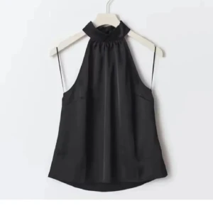 Svart halterneck linnetopp i satin - Från ginatricot Snygg svart halterneck topp i glansigt satinmaterial. Toppen är ärmlös med hög krage och lätt rynk vid halsen för en chic look. Perfekt att styla med smycken och jeans för en trendig outfit.