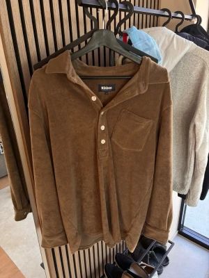 Brun frottéskjorta från Nikben - Mjuk brun skjorta från Nikben i frotté med lång ärm, bröstficka och knappar framtill. Perfekt för en avslappnad och trendig look.