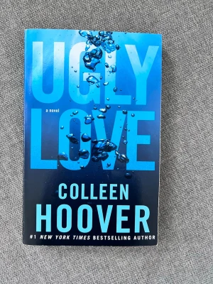 Ugly Love av Colleen Hoover - En gripande roman av Colleen Hoover med blått omslag och stora bokstäver. Boken handlar om Tate och Miles, och deras komplicerade relation där känslor och regler sätts på prov. Perfekt för dig som gillar romantik och drama med djupare teman.