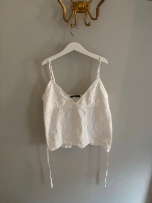 Topp från brandy melville🫶🏼 - Snygg vit linnetopp med smala axelband och v-ringning. Toppen har en luftig passform och knytband i sidorna för extra detalj. Perfekt för varma dagar och enkel att styla till olika looks.