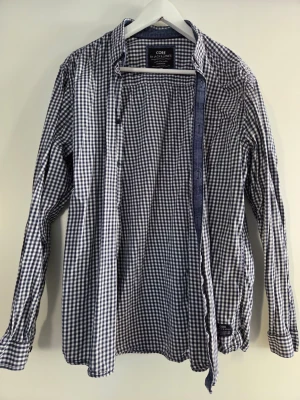 Rutig skjorta från Jack & Jones - Snygg långärmad skjorta från Jack & Jones i blåvitt rutigt mönster. Skjortan har klassisk krage, knäppning framtill och är tillverkad i bomull. Perfekt för en avslappnad men stilren look.