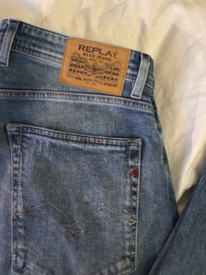 Blå jeans från Replay Grover 33x30 - Säljer ett par snygga blå jeans från Replay, modell Grover. Jeansen har klassisk femficksdesign, ljus tvätt och detaljer som Replay-logga på fickan och bak på linningen. Tillverkade i bomull med en skön passform och raka ben. Perfekta för en avslappnad stil.