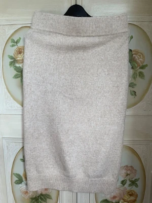 Beige stickad kjol med slits - Mysig beige stickad kjol med bred resår i midjan och en liten slits bak. Kjolen har en rak passform och är perfekt för dig som gillar en enkel men stilren look.