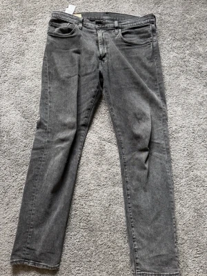 Grå Levi's jeans med rak passform - Snygga grå jeans från Levi's med klassisk femficksdesign och rak passform. Jeansen har en läderpatch bak i midjan och den ikoniska röda Levi's-taggen på bakfickan. Tillverkade i slitstark denim som ger en cool och avslappnad vibe.
