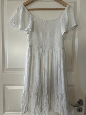 Vit sommarklänning med volangärm - Superfin vit klänning med smockad överdel och vida volangärmar. Klänningen har en luftig kjol i flera lager och är tillverkad i ett lätt bomullstyg. 💕💕