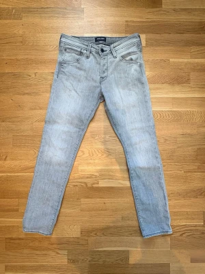 Ljusgrå slim fit jeans - Säljer ett par ljusgrå slim fit jeans från Jack & Jones. Jeansen har klassisk femficksdesign, svarta detaljer vid midjan och raka ben. Perfekta för en clean och modern look. W29 L30