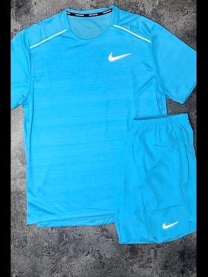 Blått träningsset från Nike - Snyggt blått träningsset från Nike med t-shirt och shorts. Båda plaggen har Nike-logga i vitt och är gjorda i ett lätt och snabbtorkande material. Perfekt för träning eller sportaktiviteter.
