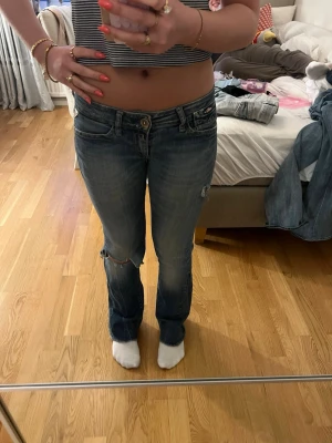 Blåa lågmidjade jeans från Replay - Säljer ett par blåa lågmidjade jeans från Replay med slitningar och hål på ena knät. Jag är 160 och jeansen är stl xs