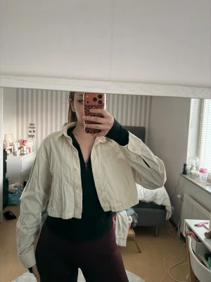 Croppad beige skjorta med knappar - Snygg croppad skjorta i beige med klassisk krage och knäppning framtill. Skjortan har långa ärmar och en loose passform, perfekt för en chill och trendig look. Passar till både jeans och kjol för en cool stil.