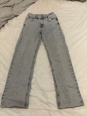 Ljusgrå raka jeans med mid waist - Snygga ljusgrå jeans med raka ben och mid midja. Klassisk femficksmodell med bälteshällor och dragkedjegylf. Jeansen har en avslappnad passform och är tillverkade i denim. W26 L30. Knappt använda