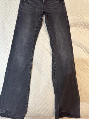 Grå bootcut jeans från Gina Tricot - Säljer ett par grå bootcut jeans från Gina Tricot med snygga slitningar och kontrastsömmar. Jeansen har klassisk femficksmodell och breda hällor för bälte. Perfekta för dig som gillar en avslappnad men trendig look.