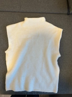Vit stickad väst med polokrage - En enkel och stilren vit stickad väst med hög polokrage. Västen har raka axlar och ärmlösa sidor, perfekt att bära över en skjorta eller tröja för en clean look. Nästan helt ny, aldrig andvänd då den ej passar mig tyvärr, kan definitivt diskutera pris vid snabb affär!🥰