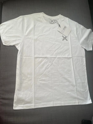 Vit t-shirt från Kenzo med logga - Snygg vit t-shirt från Kenzo med diskret svart logga tryckt på bröstet. Klassisk rund halsringning och korta ärmar. Tillverkad i mjuk bomull som känns skön mot huden. Perfekt för dig som gillar stilrena och trendiga plagg.