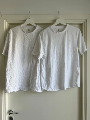 Två vita basic t-shirts i bomull - Säljer två klassiska vita t-shirts i bomull med rund hals och kort ärm. Perfekta som basplagg och enkla att matcha till allt. T-shirtsen har en avslappnad passform och är riktigt sköna att bära.