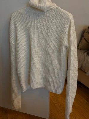 Vit stickad polotröja - Mysig vit stickad polotröja med ribbad struktur och långa ärmar. Tröjan har en hög polokrage som ger extra värme och en avslappnad passform. Perfekt för kalla dagar och enkel att matcha med olika outfits.