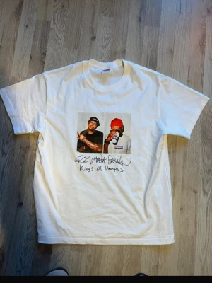 Vit Supreme Kings of Memphis t-shirt - Vit t-shirt från Supreme med tryck av två personer på bröstet och texten 'Kings of Memphis' under bilden. Klassisk passform och rund hals. Perfekt för dig som gillar streetwear och unika prints.