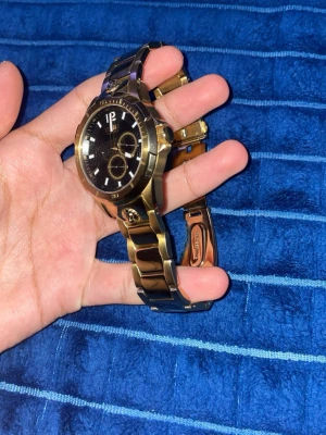 Versus Versace guldig klocka - Snygg klocka från Versus Versace med guldig länk och svart urtavla. Klockan har flera små urtavlor och tydliga index, samt Versus-logga på länken. Perfekt accessoar för dig som vill sticka ut med stil.