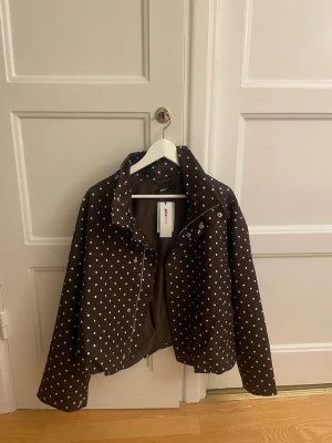 Brun prickig jacka från Gina Tricot - SLUTSÅLD Snygg brun jacka från Gina Tricot med vita prickar och hög krage. Jackan har dragkedja och snygga knappar. Perfekt för våren hösten. Den är använd en gång och har prislapp kvar 