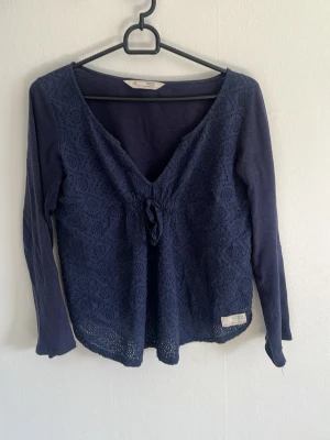 Mörkblå blus från Odd Molly - Supersnygg mörkblå blus från Odd Molly med broderad spets framtill och v-ringning med knyt. Långärmad modell i mjukt bomullstyg, perfekt för en trendig och avslappnad look.
