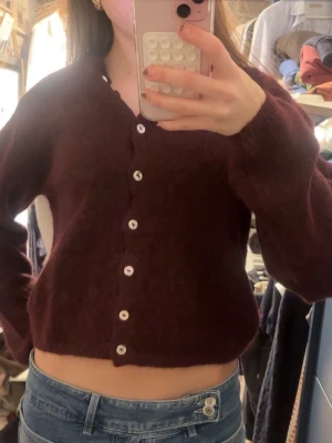 Vinröd cropped kofta med vita knappar - Vinröd kofta i cropped modell med långa ärmar och vita knappar. Koftan har en enkel design och är perfekt att slänga över ett linne