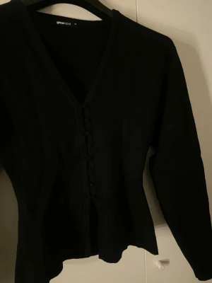 Svart tröja med knappar från Gina Tricot - Svart tröja från Gina Tricot med v-ringning och dekorativa knappar framtill. Koftan har lång ärm och är tillverkad i mjukt stickat material. 