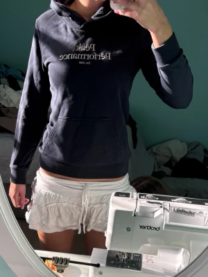 Svart hoodie från Peak Performance - Snygg marinblå hoodie från Peak Performance med broderad logga och text på bröstet. Klassisk känguruficka framtill och ribbade muddar vid ärmar och nederkant. Perfekt för en avslappnad och sportig stil. Mjuk och skön bomullsblandning.