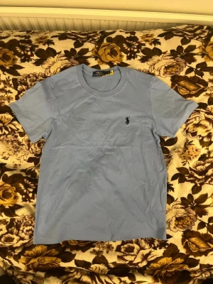 Ljusblå t-shirt från Polo Ralph Lauren - Snygg ljusblå t-shirt från Polo Ralph Lauren med klassisk passform och den ikoniska loggan broderad på bröstet. Tillverkad i mjuk bomull och har korta ärmar. Perfekt till jeans eller shorts för en clean och stilren look.