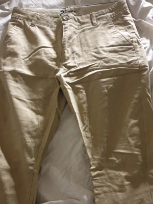 Beige chinos med regular fit - Snygga beige chinos med regular fit och klassisk design. Byxorna har framfickor, bälteshällor och en bakficka med diskret söm. Tillverkade i ett mjukt bomullsmaterial som ger en skön känsla och stilren look.