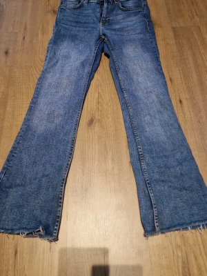 Blå bootcut jeans - Ett par blå bootcut jeans med rå, fransig kant längst ner. Klassisk femficksmodell med normalhög midja och dragkedja. Jeansen har en avslappnad passform och är tillverkade i denim. Perfekta för en trendig och avslappnad stil.