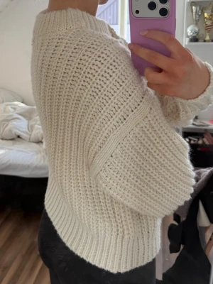 Krämvit chunky stickad tröja - Säljer en chunky stickad tröja i krämvitt med bred ribbstickad kant vid hals, ärmslut och nederkant. Tröjan har en avslappnad passform och grovstickad struktur som ger en mysig och trendig look. Perfekt för kyliga dagar.